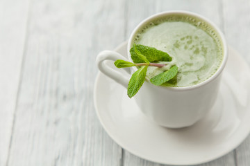 cup of hot matcha green tea with branch of mint on a grey background,close up