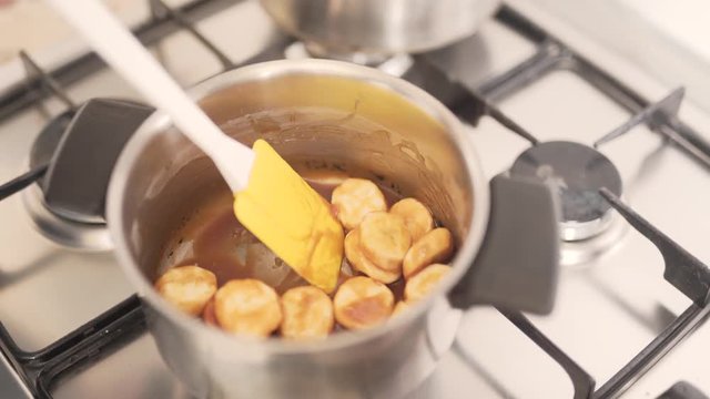 Close-up scene of a woman who is making a cream for a cake from bananas in melted chocolate. Woman is making them caramelized.