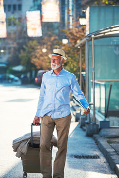Happy Senior tourist man with suitcase in city.