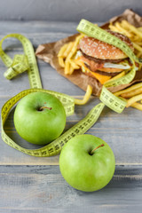 green apples on the background of a burger and fries. Sewing Tape Measures on the food. concept of opposition  healthy food and junk food. selective focus