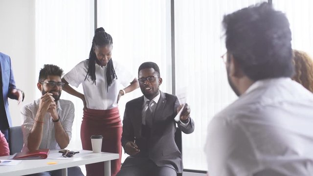 Young interracial coworkers sitting at open space office together, working on laptops, collaborating in modern office interior with panoramic windows. Teamwork Concept