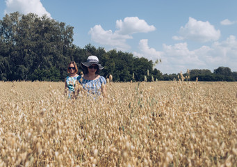 female friends in sunglasses walking through oat field