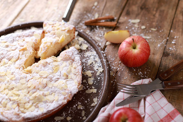 Sweet homemade apple pie on a plate with fresh apples and cinnamon sticks on a rustic wooden table