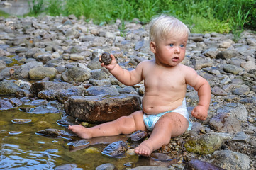 Baby in a diaper throws stones into the water, Blonde in the water