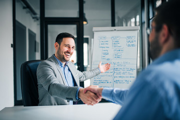 Smiling millennial businessman handshaking coworker, celebrating successful teamwork.