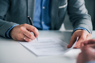 Businessman sitting at desk holding and pen signing contract paper, employment or partnership agreement.