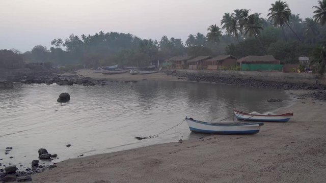 Panning shot across row of grass thatched colourful beach huts on the shoreline of Indian, Goa beach. View of coastal waters in foreground.