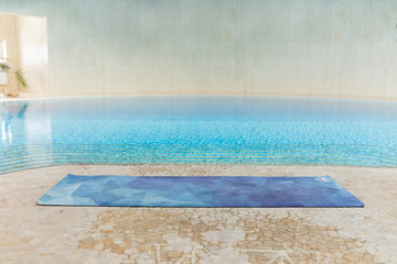 blue yoga mat in gym interior after a yoga class on floor near a pool, close up
