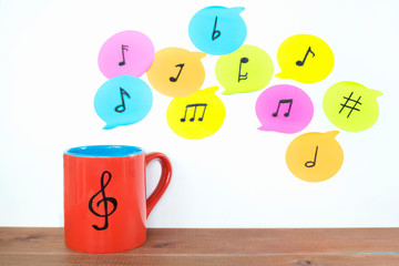 Red mug with drawn musical key and different notes on the light background. 