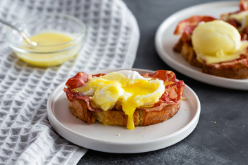 Eggs Benedict- toasted English bread, parm ham, poached eggs with hollandaise sauce and lemon on gray background