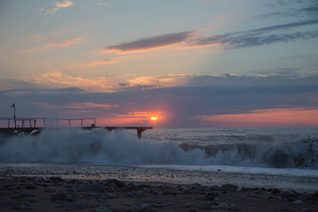 sun setting over Batumi beach Jetty, as powerful waves roll in, and a very colorful sky is reflected on the beach