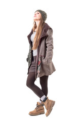 Fototapeta premium Stylish hipster girl in winter clothes wearing beanie and hooded coat looking at camera with attitude. Full body isolated on white background. 