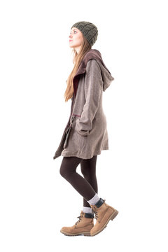 Side View Of Stylish Young Hipster Woman Wearing Beanie And Hooded Coat Walking And Looking Up. Full Body Isolated On White Background. 