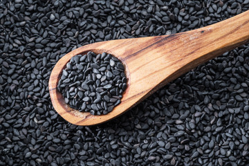 Black sesame seeds in the wooden spoon. Sesame seeds in the dish at the background. Top view.