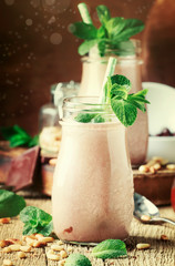 Chocolate mint smoothies or milk cocktails with cedar nuts in glass bottles on old wooden kitchen table background, selective focus