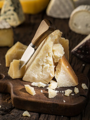 Piece of Parmesan cheese  on the wooden board. Assortment of different cheeses at the background.