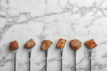 Forks with fried meat fondue pieces on marble background, top view. Space for text