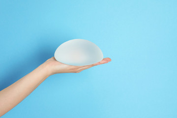 Woman holding silicone implant for breast augmentation on color background, space for text. Cosmetic surgery