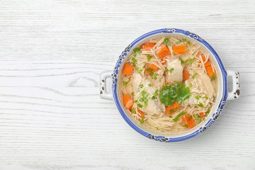 Homemade chicken soup served on wooden background, top view with space for text