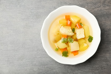 Homemade chicken soup in dish on grey background, top view with space for text