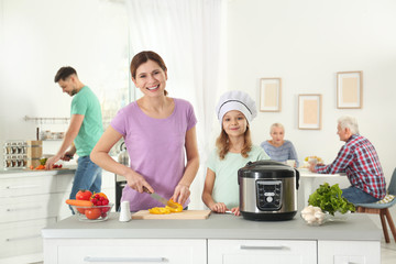 Mother and daughter preparing food with modern multi cooker in kitchen