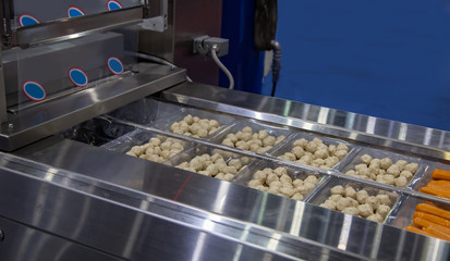Meat ball and sausage in tray on linear food heat sealing machine. Food industry product