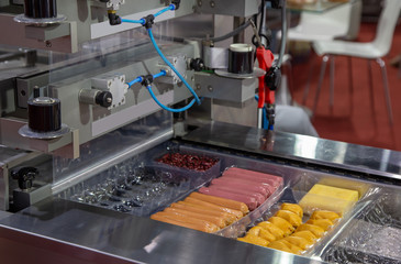 Sausage in plastic tray on food heat sealing machine. Food industry product