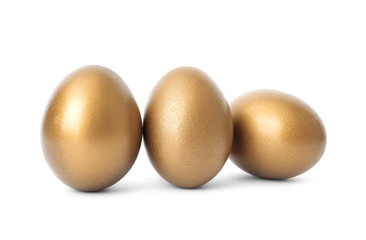 Three shiny golden eggs on white background