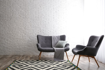 Stylish sofa and armchair near brick wall in modern living room interior. Space for text