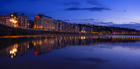 Naklejka premium SAN SEBASTIAN, SPAIN - March 06, 2019: The buildings of the city are reflected in the water of La Concha beach in the city of Donostia