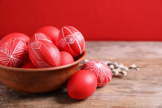 Wooden bowl with red painted Easter eggs on table against color background, space for text