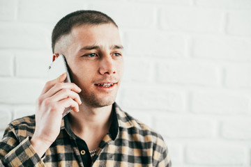 A young man stands with a mobile phone and talks smiles and laughs in a plaid shirt