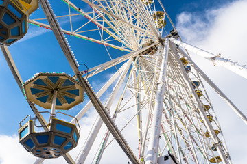 Ferris wheel with colorful gondolas in a funfair, against a beautiful blue sky with white clouds.