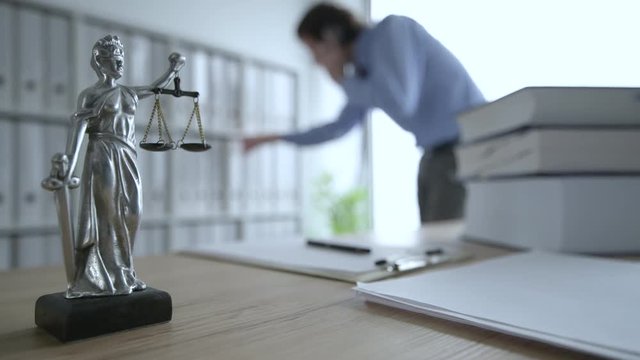 Lawyer talking on mobile phone in law office, selective focus on statue of Lady Justice