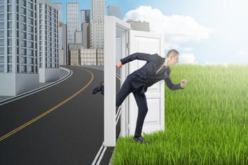 Side view of businessman running from modern city to green field through door standing alone between them with no wall.
