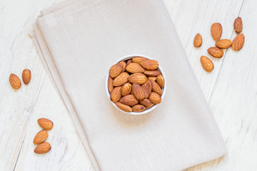 top view of Roasted Almonds in white porcelain bowl on textile napkin and white wooden table