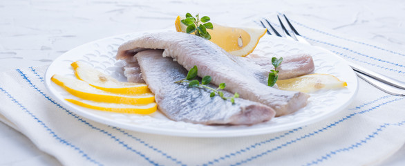 Marinated herring fillet on a white plate with lemon and onion. Served table and the traditional spring delicacy of the Netherlands. Typical cooking fish in Holland. Copy space.