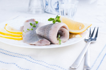 Marinated herring fillet on a white plate with lemon and onion. Served table and the traditional...