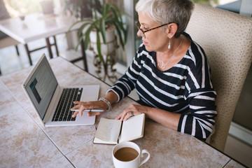 Mature beautiful woman working on her laptop at home. Elderly woman typing on her laptop while...