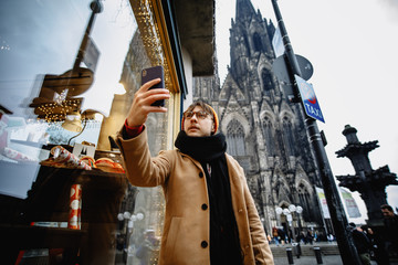 Man makes a selfie on the background of attractions. Tourist in Germany. Selfie by mobile phone looking aside. Photo of cheerful young man. 