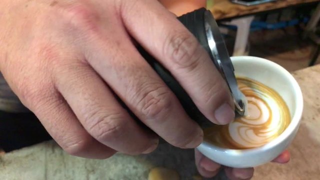 Close up hand of barista pouring latte art with espresso and milk froth in white hot ceramic cup.