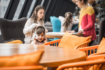 A charming little girl was sitting at a wooden table with a menu on her head in the restaurant