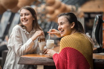 Two happy women are sitting in a cafe, drinking milkshakes,