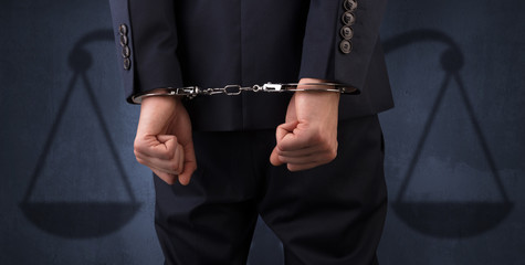 Arrested businessman in handcuffs with hands behind back and justice symbol wallpaper
