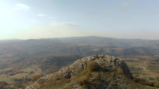 Tracking out aerial shot over rocky hill, green valley as background