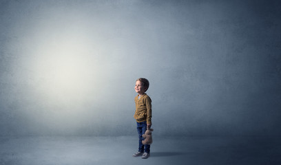 Little waggish kid staying alone in a big empty room with his plush

