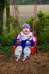 Kleinkind sitzt in einer Kinderschaukel im Garten