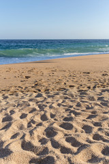 Fototapeta na wymiar Many footprints o a beach sand with quiet water in Costa Brava, Catalonia