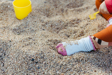 Baby foot covered by a sock playing on a the beach sand with a yellow pot