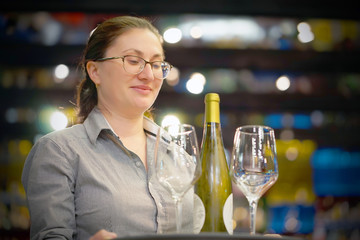Waitress carries a bottle of white wine with wine glasses on a tray to the customer of the hotel restaurant. The concept of service.